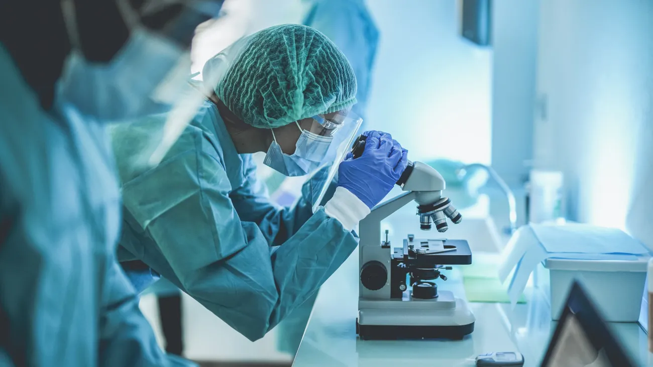 scientist in protective gear examining samples under a microscope in a lab