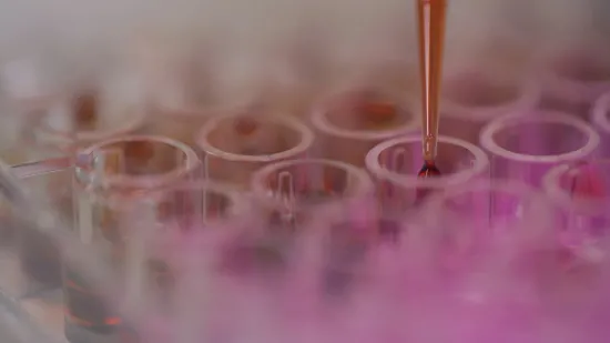 A pipette dropping red liquid into a tray of test tubes filled with pink solution.