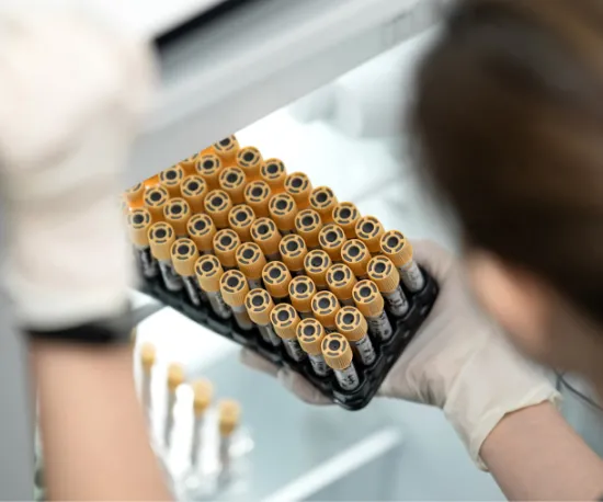 Lab technician handling a tray of blood sample vials inside a medical refrigerator.